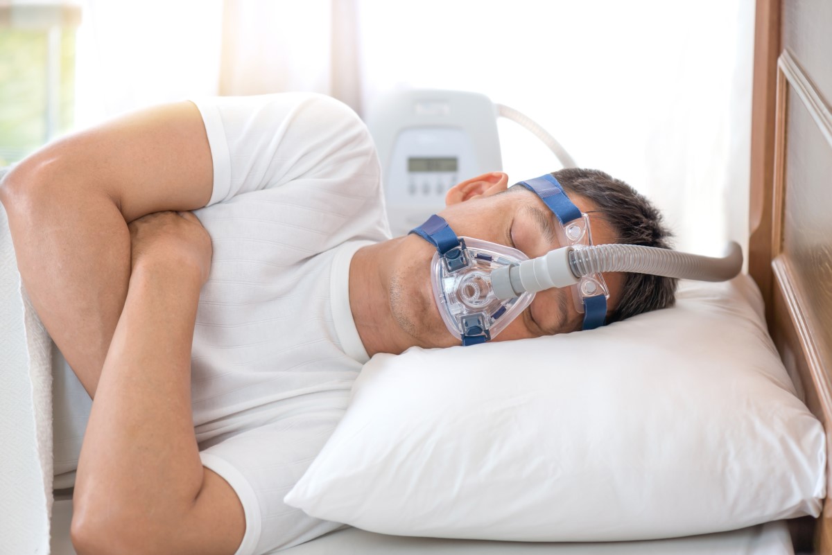 Maska CPAC do utrzymywania ciśnienia podczas snu. Źródło: Getty Images Maska CPAP na twarzy mężczyzny z bezdechem sennym