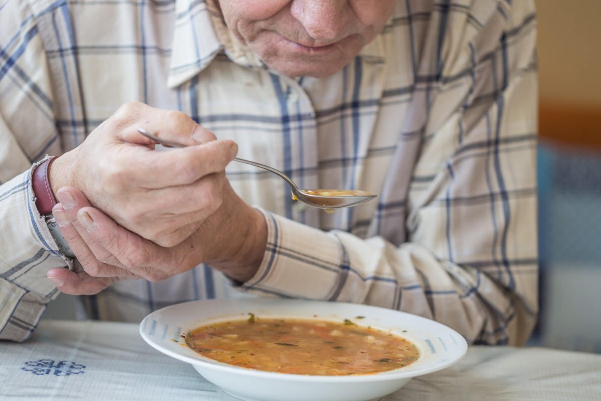Drżenie powoduje problemy w wykonywaniu codziennych czynności. Źródło: Getty Images Mężczyzna je zupę i trzyma się za rękę, aby zapobiec drżeniu w chorobie Parkinsona