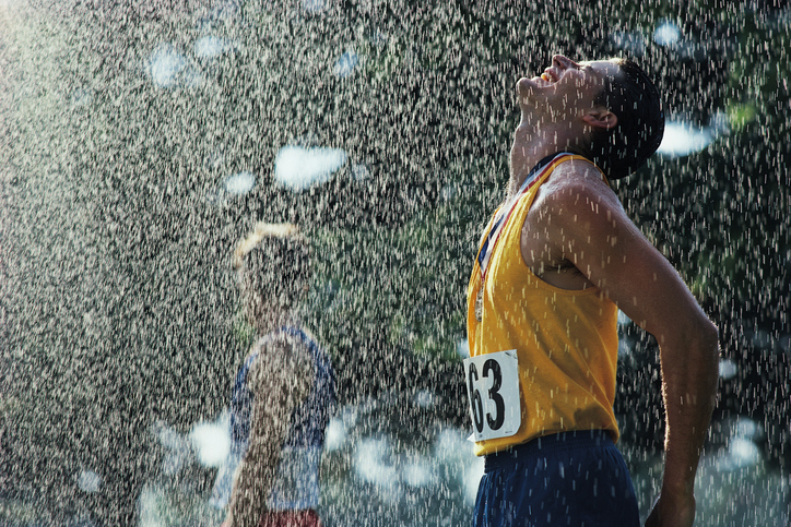 Nawet uprawianie sportu w każdych warunkach pogodowych jest częścią procesu hartowania. Źródło: Thinkstock Sportowiec po przekroczeniu linii mety. Pada deszcz. Jego głowa jest odwrócona do góry w kierunku spadających kropel. Ma zamknięte oczy, na szyi nosi medal. Ma na sobie żółty podkoszulek z numerem 63 i niebieskie szorty.