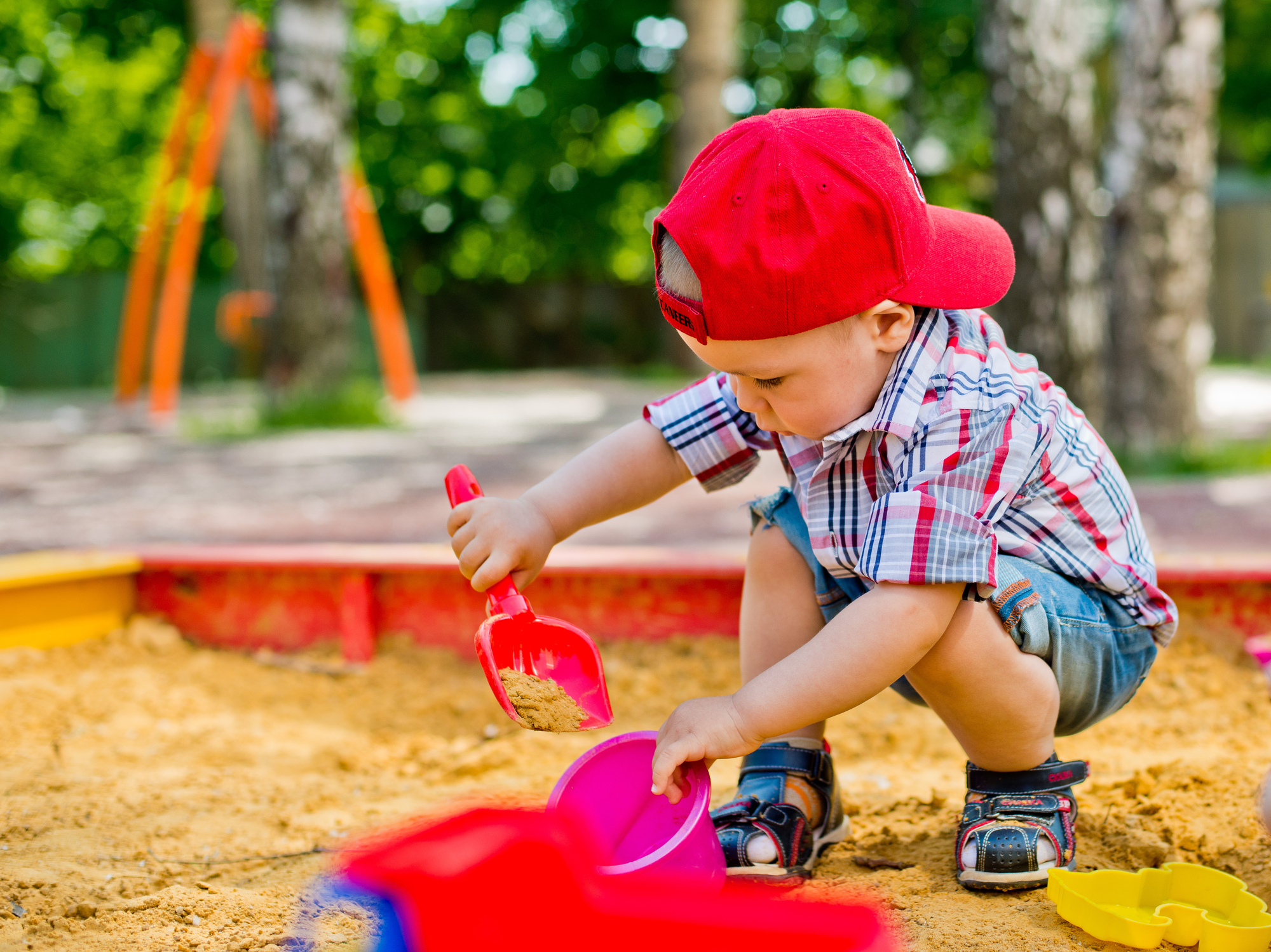 Zabawa w piasku rozwija nie tylko umiejętności dzieci. Zdjęcie: Thinkstock Chłopiec nabierający piasek łopatką do wiaderka w piaskownicy.