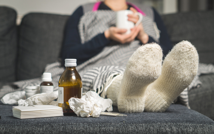 Katar, stan zapalny, obrzęk, angina - to wszystko może Cię zaskoczyć, gdziekolwiek jesteś. Źródło: Thinkstock chora kobieta leży w łóżku z ciepłymi skarpetami, tabletkami i syropami obok niej