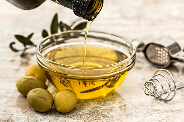 Oliwa z oliwek jest ważnym składnikiem diety śródziemnomorskiej. Źródło: Pixabay Oliwa z oliwek wlewana jest do szklanej miski ze szklanej butelki. Wokół miski umieszczane są zielone oliwki.