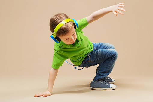 Dzieciak w zielonej koszulce ze słuchawkami na uszach tańczy break dance.