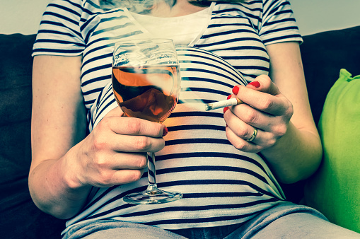 Kobieta w ciąży w koszulce w paski z papierosem i kieliszkiem wina