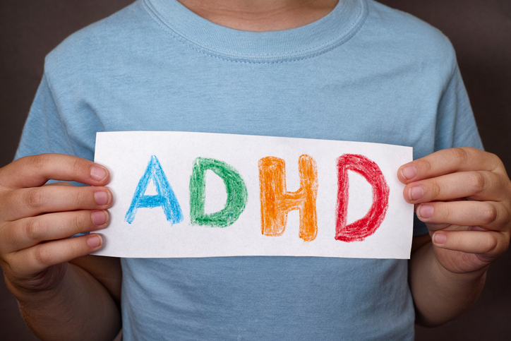 Chłopiec trzyma tabliczkę z kolorowym napisem ADHD