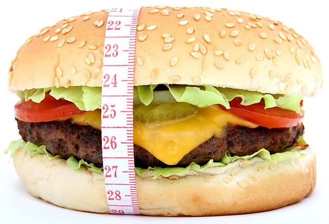 Niewłaściwa dieta jest jedną z przyczyn nadwagi. Zdjęcie źródłowe: Getty Images hamburger z owiniętą wokół niego miarą krawiecką