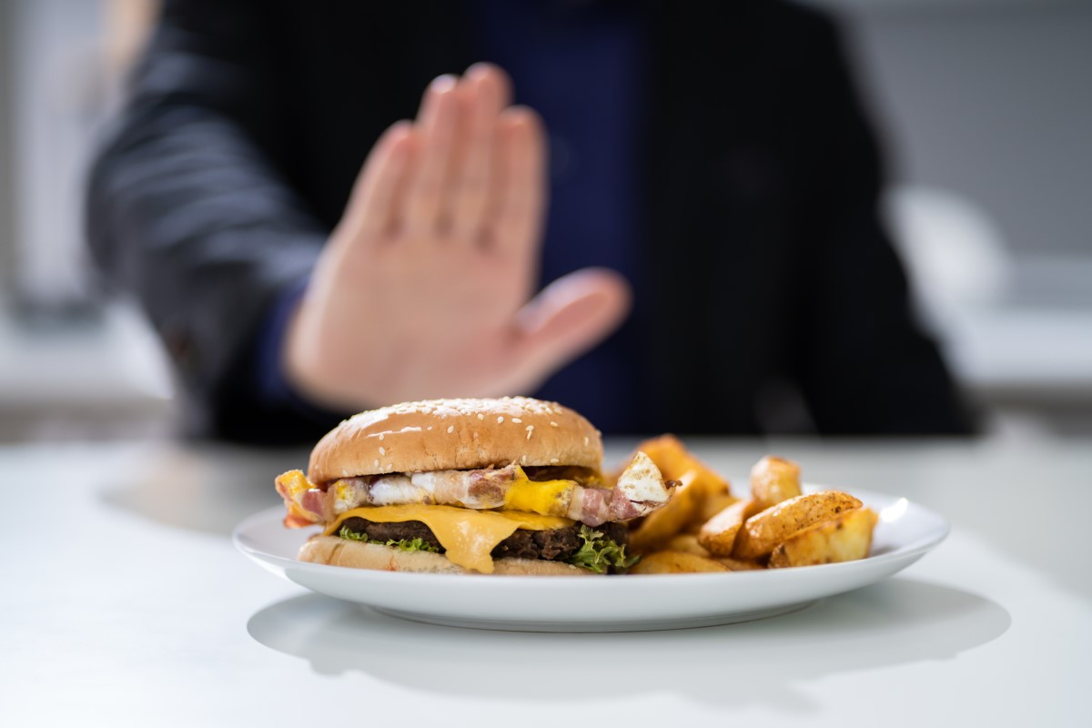 Niewłaściwe jedzenie i błędy dietetyczne jako częsta przyczyna zgagi. Źródło zdjęcia: Getty Images Nieodpowiednie jedzenie jako przyczyna zgagi - hamburger na talerzu, którego mężczyzna odmawia