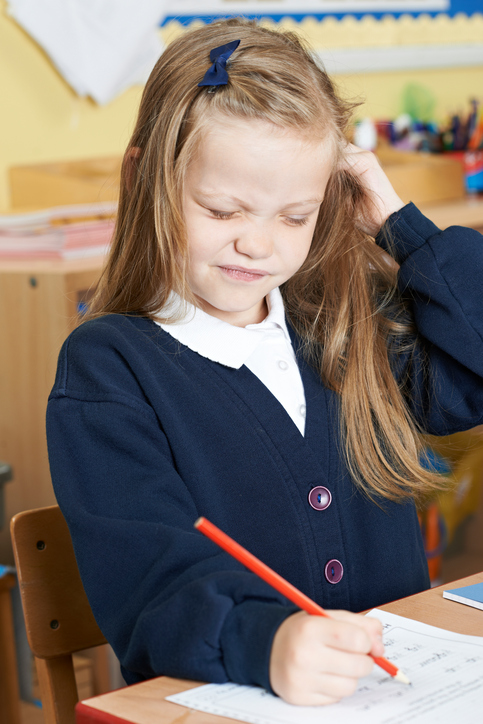 Wszy u dzieci powodują utratę koncentracji. Źródło zdjęcia: Thinkstock photos Mała dziewczynka siedzi w szkole ze swędzącą głową, prawdopodobnie wszy we włosach, blond włosy, siedzi i pisze