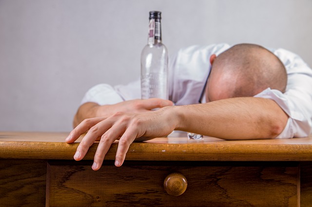 Alkoholizm przyczyną zaburzeń nastroju, mężczyzna leży na stole trzymając pustą butelkę po alkoholu, alkoholik
